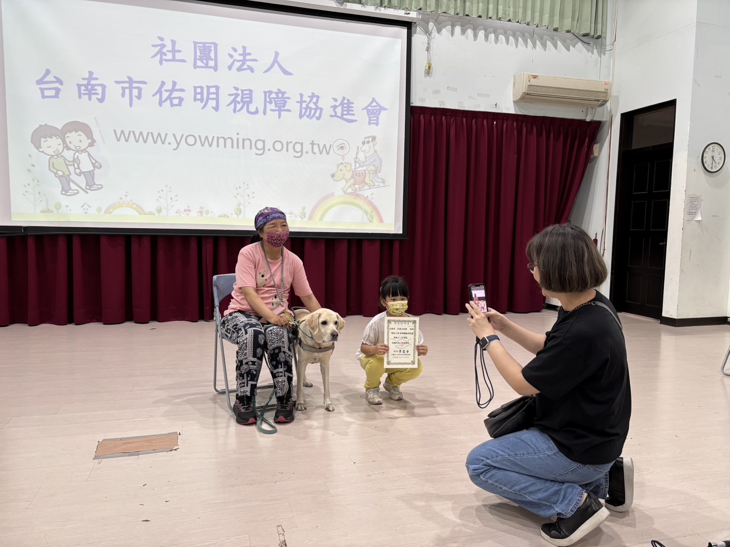 一位女生在幫導盲犬和主人、小朋友拍照